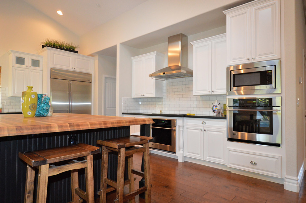 Mid-sized modern single-wall eat-in kitchen in Toronto with an undermount sink, shaker cabinets, white cabinets, wood benchtops, white splashback, subway tile splashback, stainless steel appliances, medium hardwood floors, with island and brown floor.
