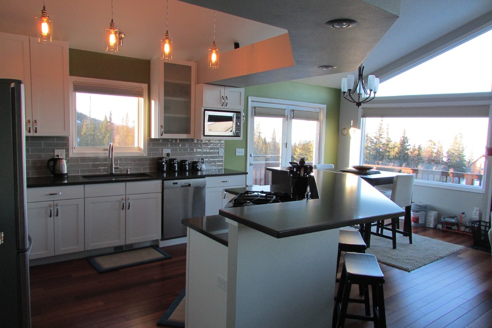Mid-sized transitional l-shaped medium tone wood floor and brown floor eat-in kitchen photo with a double-bowl sink, recessed-panel cabinets, white cabinets, gray backsplash, stainless steel appliances, an island and subway tile backsplash