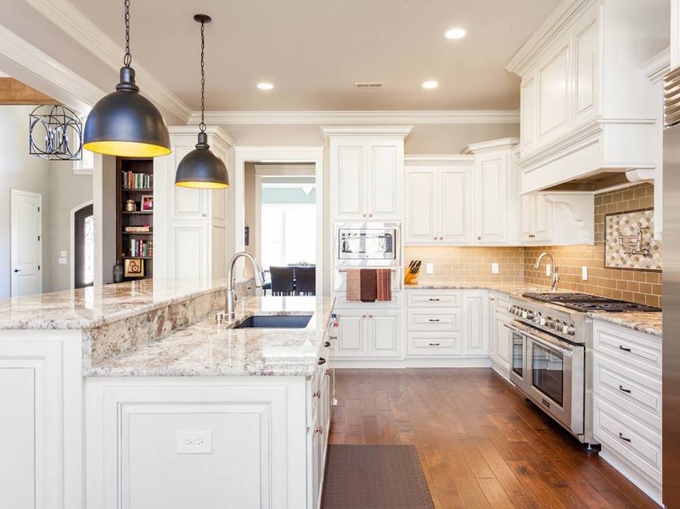 Example of a mid-sized transitional l-shaped medium tone wood floor and brown floor open concept kitchen design with an undermount sink, beaded inset cabinets, white cabinets, granite countertops, gray backsplash, subway tile backsplash, stainless steel appliances, an island and multicolored countertops