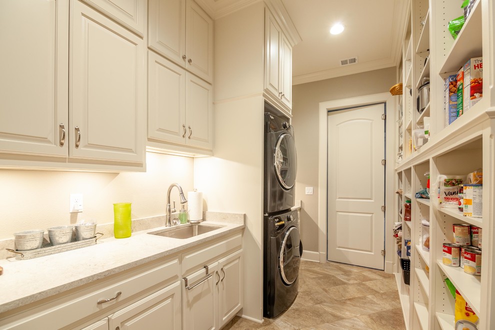 Expansive country galley utility room in Kansas City with an undermount sink, raised-panel cabinets, white cabinets, quartz benchtops, grey walls, ceramic floors, a stacked washer and dryer, beige floor and white benchtop.