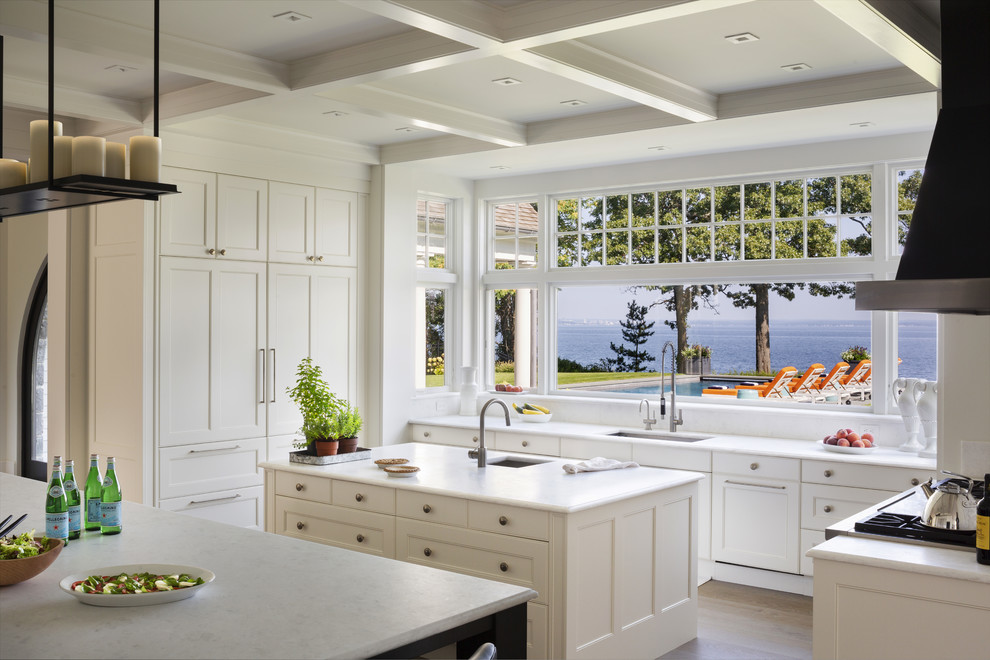 Design ideas for a beach style u-shaped kitchen in New York with an undermount sink, recessed-panel cabinets, white cabinets, medium hardwood floors, multiple islands, brown floor and white benchtop.