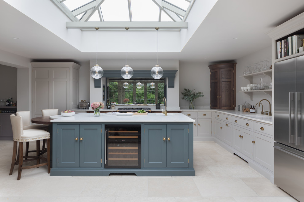 This is an example of a mid-sized transitional l-shaped kitchen in Essex with an undermount sink, shaker cabinets, grey cabinets, mirror splashback, stainless steel appliances, with island, beige floor and white benchtop.