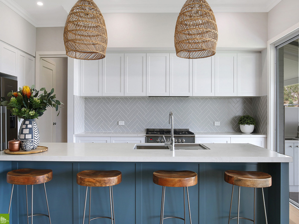 Photo of a mid-sized beach style kitchen in Wollongong with white cabinets, quartz benchtops, subway tile splashback, with island and white benchtop.