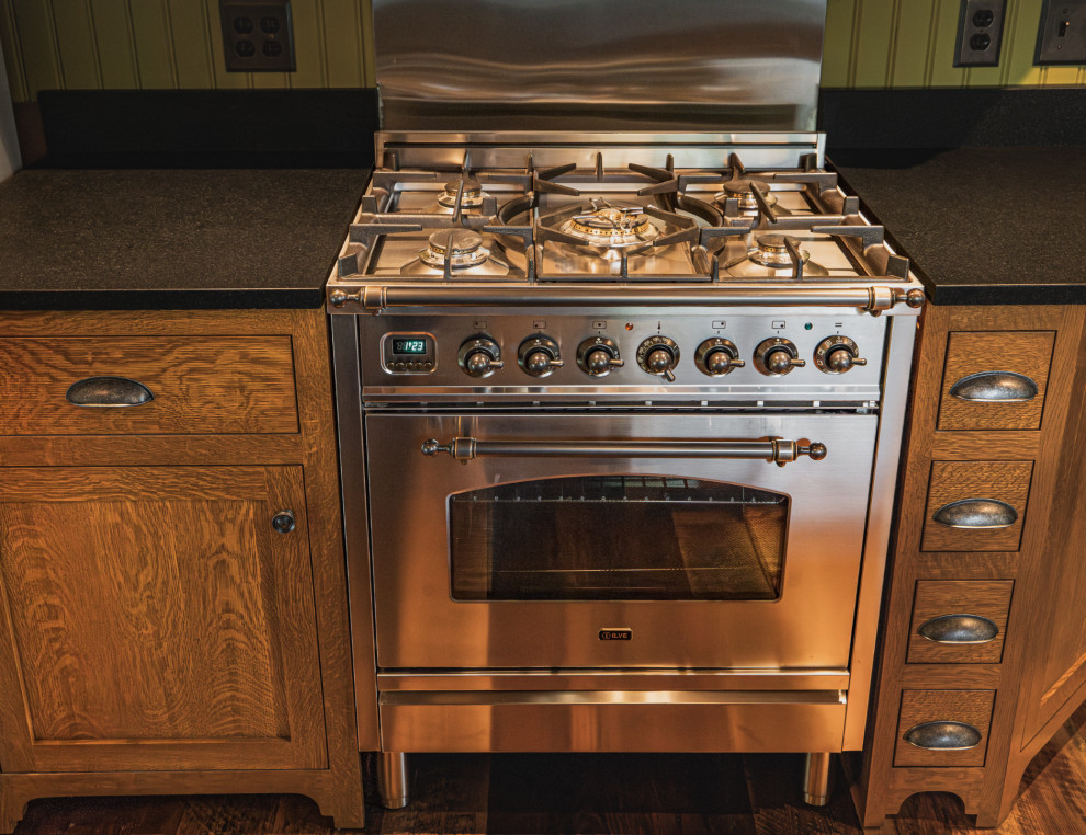Example of a mountain style medium tone wood floor and exposed beam kitchen design with an undermount sink, shaker cabinets, granite countertops, black backsplash, granite backsplash, stainless steel appliances, an island and black countertops