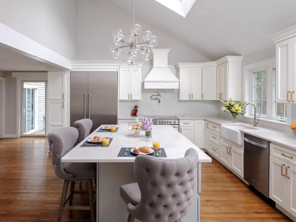 Kitchen - large transitional l-shaped medium tone wood floor and brown floor kitchen idea in Boston with white cabinets, white backsplash, an island and white countertops