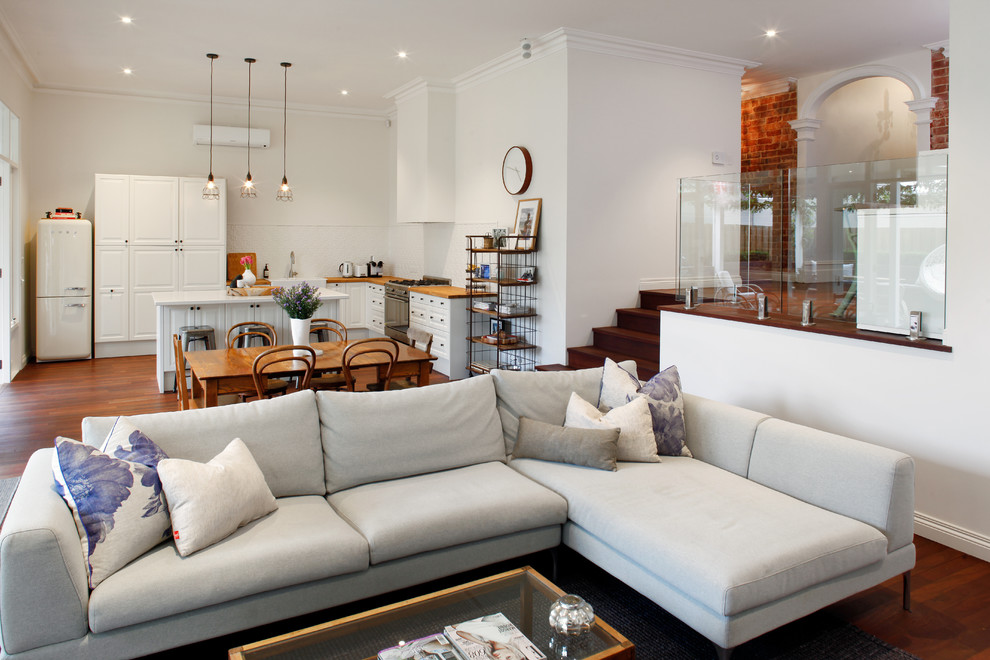 Inspiration for a mid-sized country open concept living room in Perth with white walls, medium hardwood floors, a standard fireplace, a plaster fireplace surround, a wall-mounted tv and brown floor.