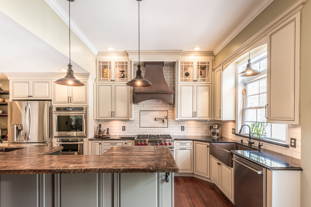 This is an example of a large country u-shaped separate kitchen in Other with a farmhouse sink, raised-panel cabinets, beige cabinets, quartz benchtops, white splashback, ceramic splashback, stainless steel appliances, medium hardwood floors, with island, brown floor and brown benchtop.