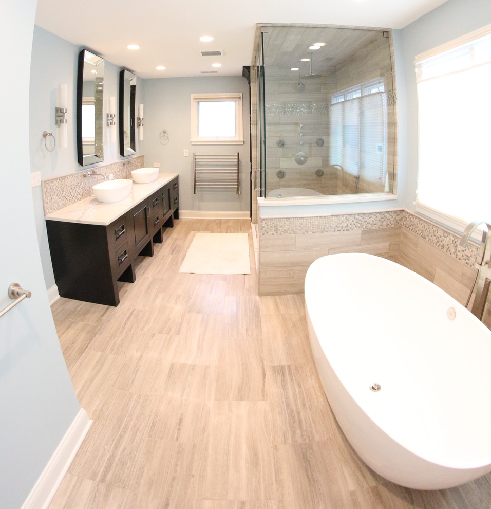 Photo of an expansive contemporary master bathroom in Chicago with recessed-panel cabinets, dark wood cabinets, a freestanding tub, a one-piece toilet, limestone, blue walls, limestone floors, a vessel sink, engineered quartz benchtops and a hinged shower door.