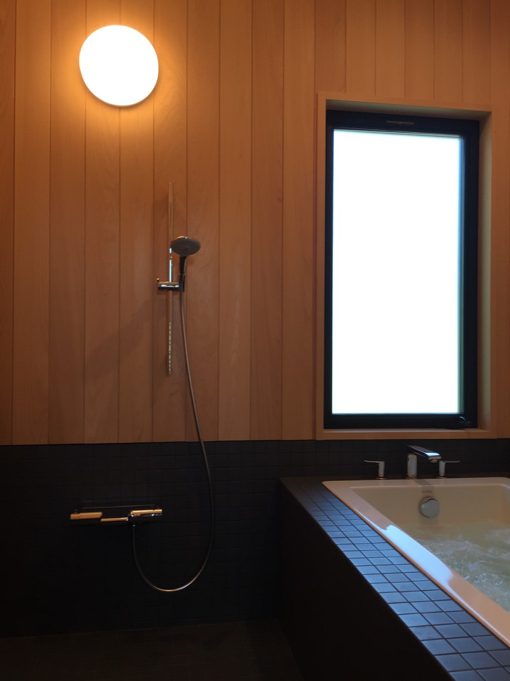 Photo of a mid-sized modern master wet room bathroom in Los Angeles with flat-panel cabinets, medium wood cabinets, a drop-in tub, a bidet, black tile, mosaic tile, brown walls, mosaic tile floors, an undermount sink, engineered quartz benchtops, black floor, a hinged shower door and black benchtops.