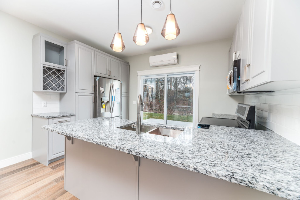 Transitional u-shaped brown floor open concept kitchen photo with an undermount sink, raised-panel cabinets, gray cabinets, granite countertops, white backsplash, ceramic backsplash, stainless steel appliances, a peninsula and multicolored countertops