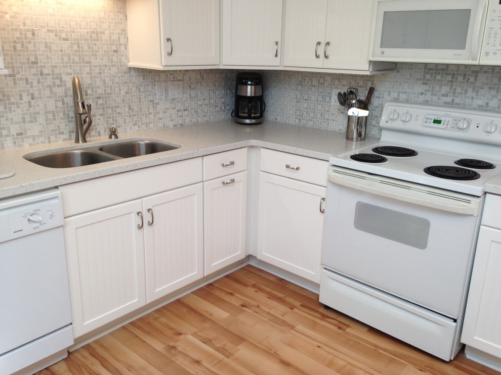Example of a mid-sized beach style l-shaped eat-in kitchen design with an undermount sink, beaded inset cabinets, white cabinets, solid surface countertops, gray backsplash, mosaic tile backsplash, white appliances and a peninsula