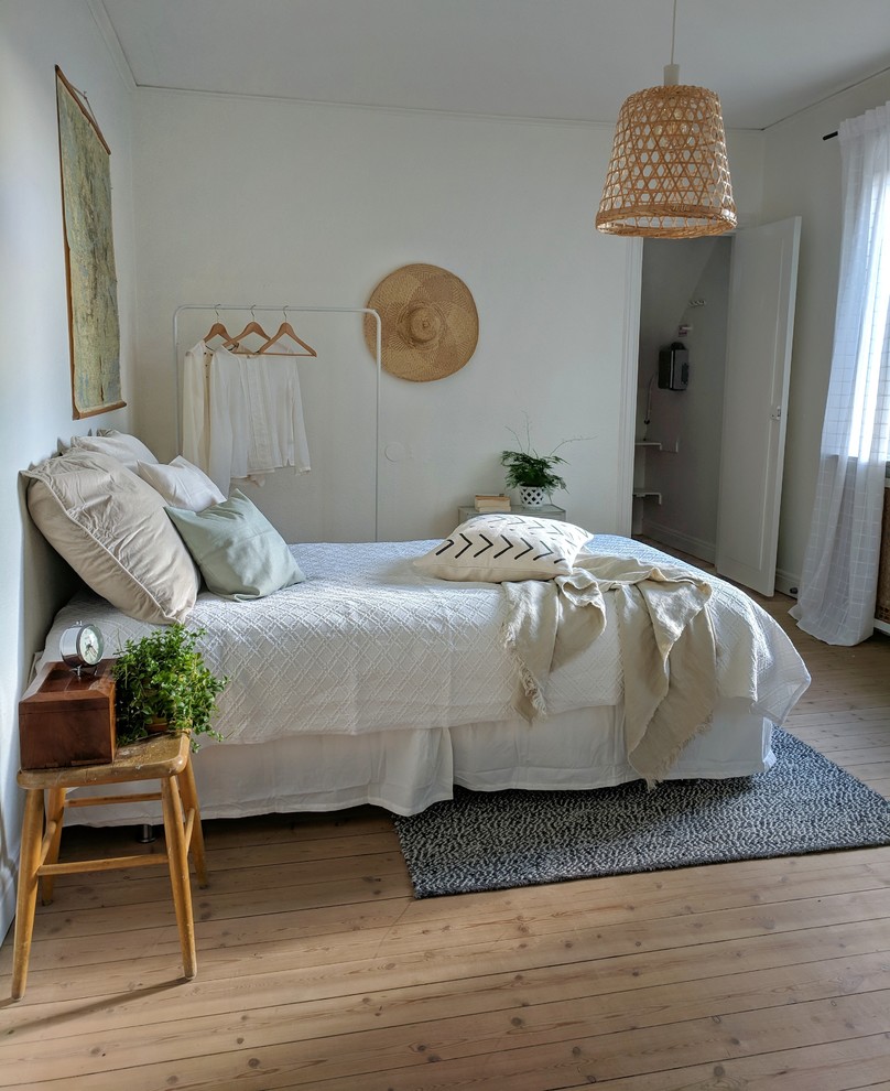 Scandinavian bedroom in Stockholm with white walls, medium hardwood floors and brown floor.