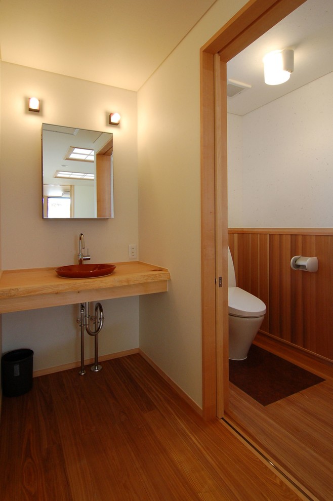 Inspiration for a small asian powder room in Other with a two-piece toilet, white walls, medium hardwood floors, a drop-in sink, wood benchtops, brown floor and beige benchtops.
