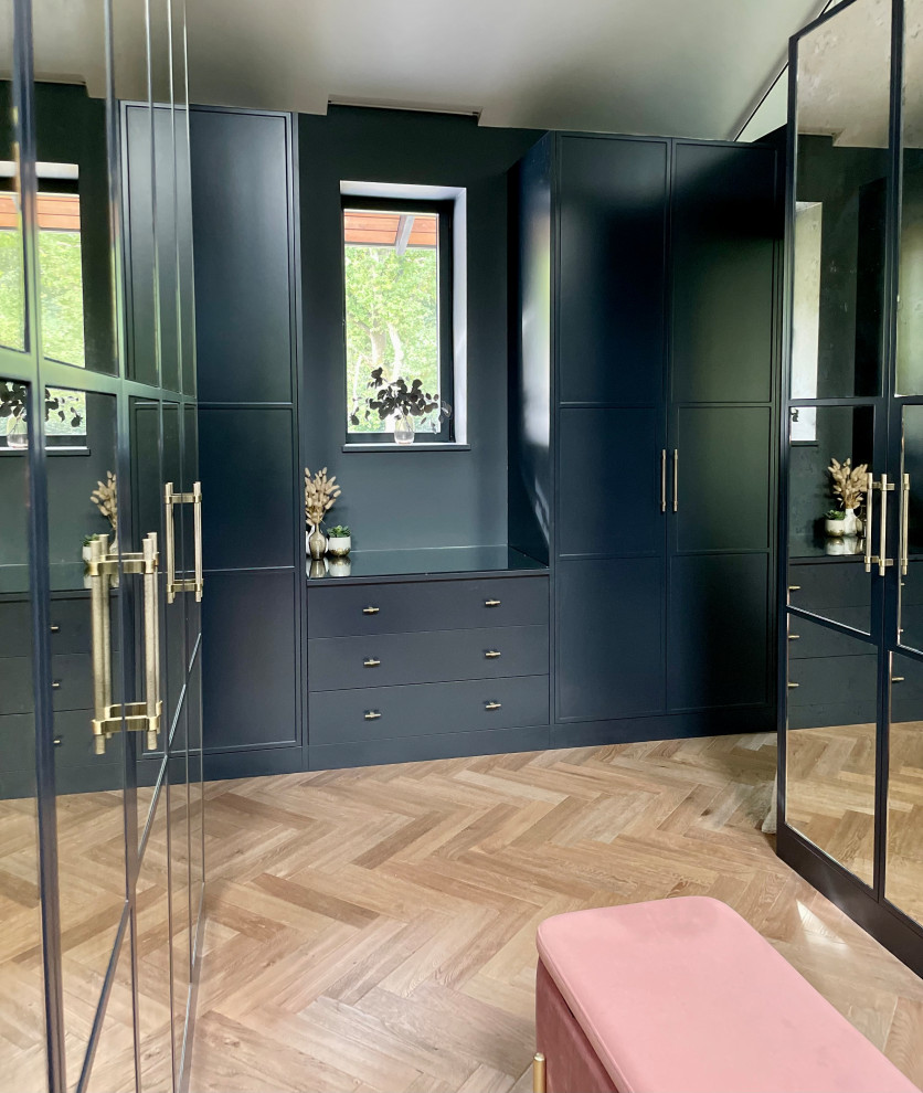 Medium sized contemporary gender neutral walk-in wardrobe in Hertfordshire with recessed-panel cabinets, grey cabinets, medium hardwood flooring, brown floors, a vaulted ceiling and feature lighting.