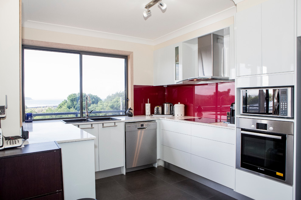 Design ideas for a mid-sized modern l-shaped eat-in kitchen in Sydney with a double-bowl sink, white cabinets, red splashback, stainless steel appliances, porcelain floors, with island and flat-panel cabinets.