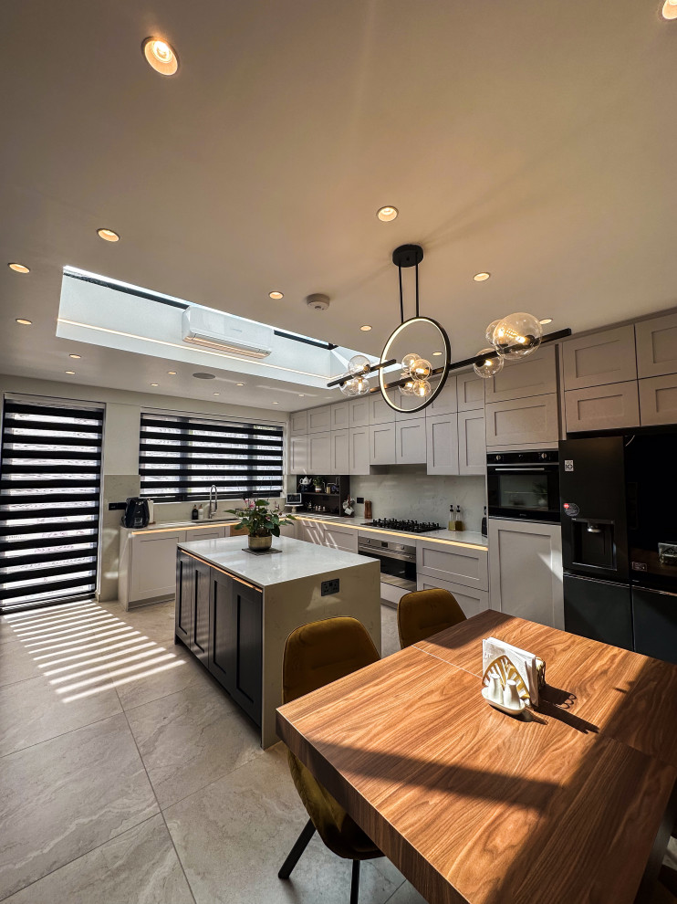 Large traditional l-shaped kitchen/diner in London with a built-in sink, shaker cabinets, blue cabinets, quartz worktops, white splashback, engineered quartz splashback, integrated appliances, porcelain flooring, an island, beige floors, white worktops and feature lighting.