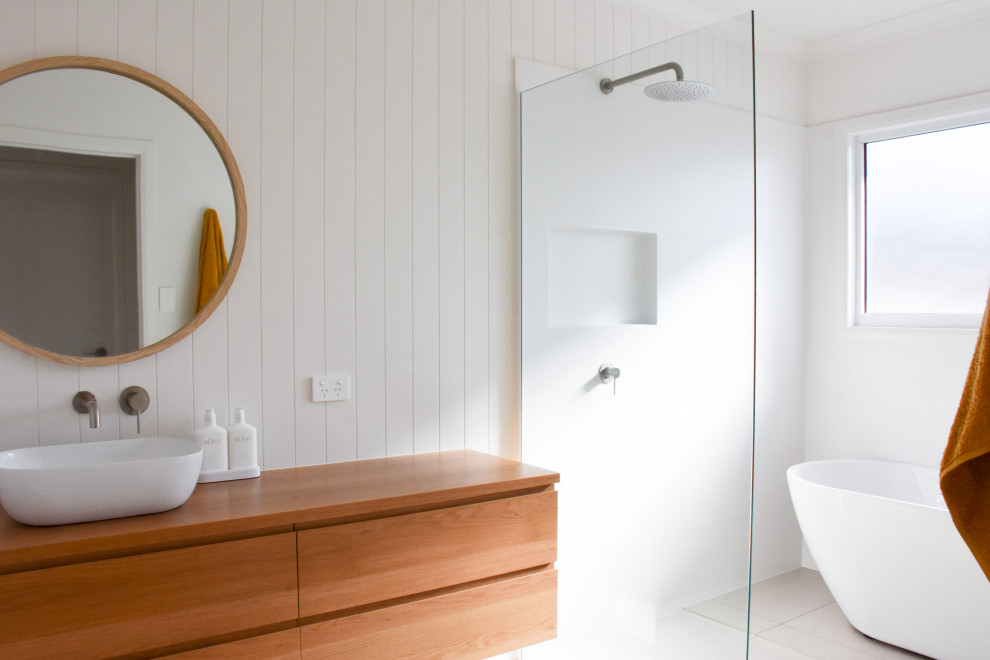Photo of a beach style bathroom in Sunshine Coast with furniture-like cabinets, light wood cabinets, white tile, white walls, wood benchtops, a single vanity and a floating vanity.