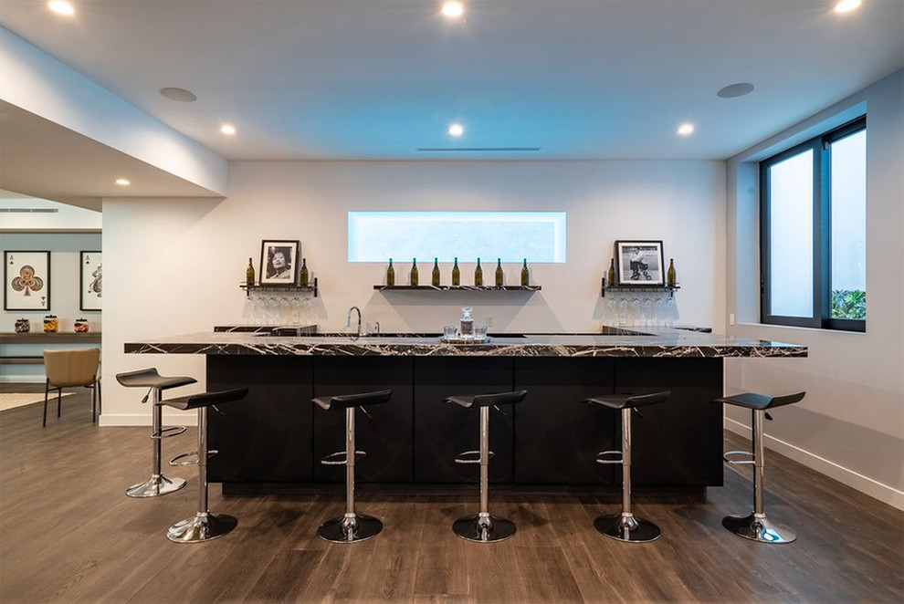 Design ideas for a large modern u-shaped seated home bar in San Diego with a drop-in sink, flat-panel cabinets, black cabinets, marble benchtops, dark hardwood floors, brown floor and black benchtop.