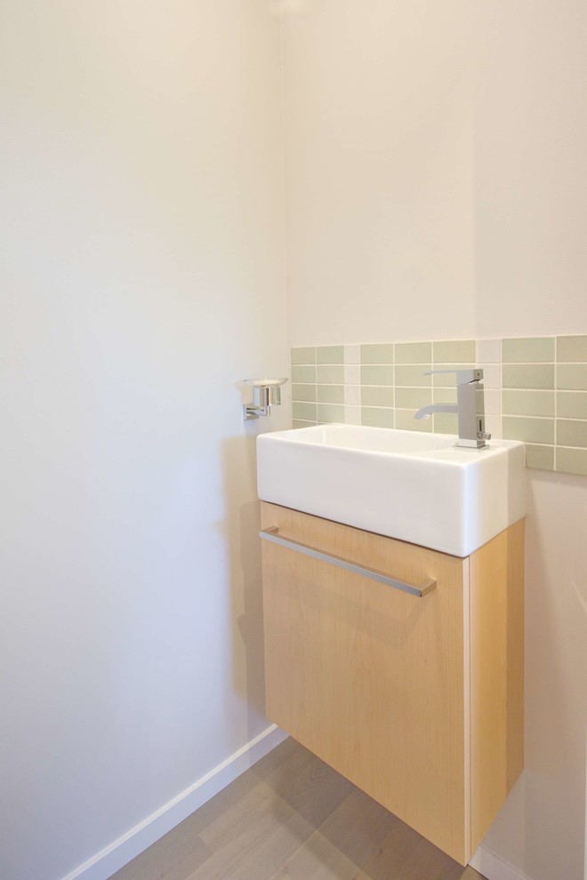 This is an example of a small contemporary powder room in San Francisco with light wood cabinets, green tile, ceramic tile, light hardwood floors, white walls, flat-panel cabinets, a vessel sink and brown floor.