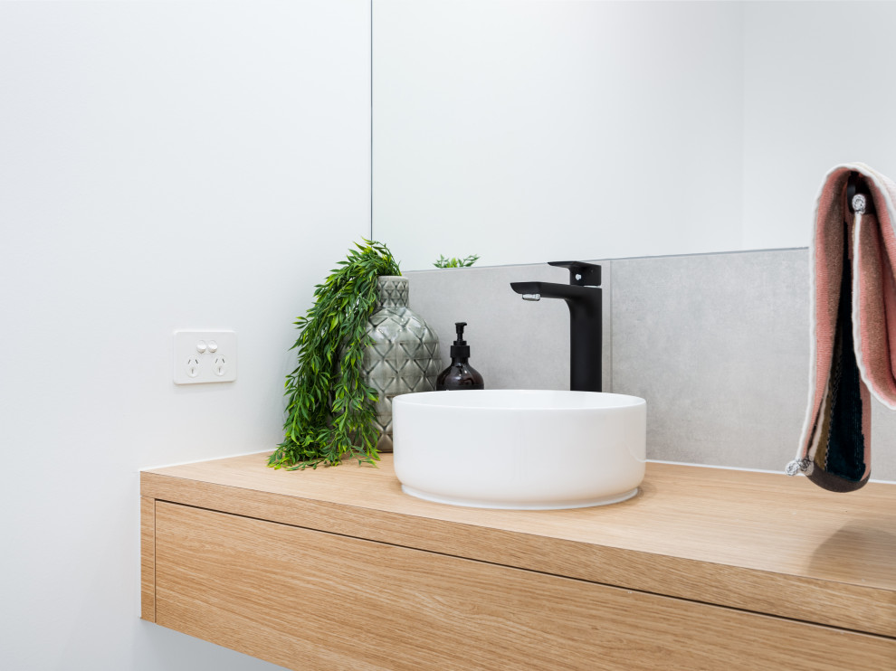 Bild på ett mellanstort funkis grå grått toalett, med skåp i ljust trä, grå kakel, keramikplattor, vita väggar, cementgolv, ett fristående handfat, träbänkskiva och grått golv