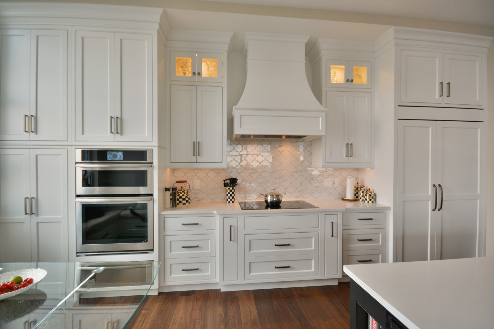 Inspiration for a transitional single-wall medium tone wood floor and brown floor open concept kitchen remodel in Toronto with an undermount sink, shaker cabinets, white cabinets, quartz countertops, white backsplash, marble backsplash, paneled appliances, an island and white countertops