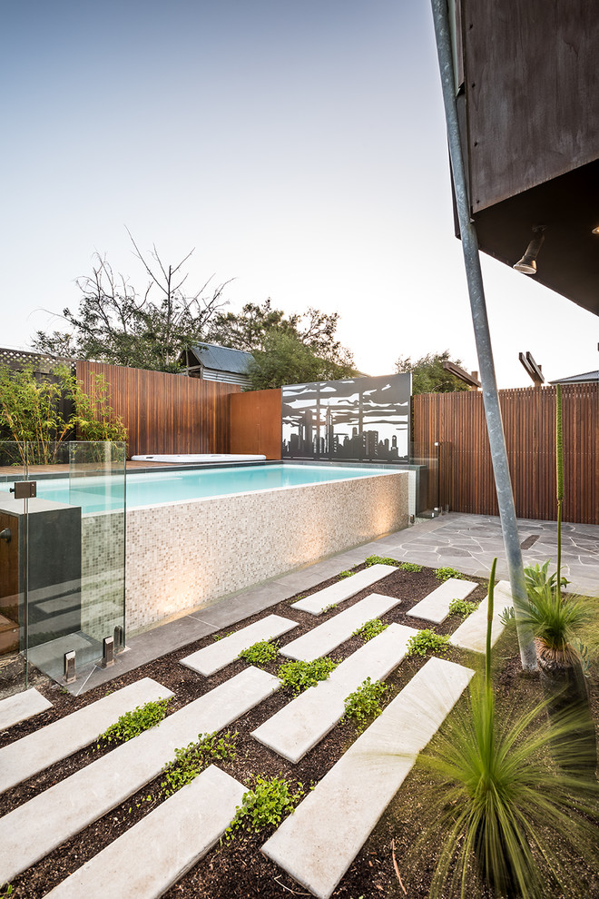 This is an example of a mid-sized contemporary backyard rectangular infinity pool in Melbourne with a hot tub and natural stone pavers.