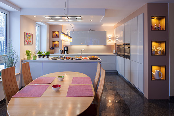 Küche in L-Form mit integriertem Waschbecken, flächenbündigen Schrankfronten, weißen Schränken, Quarzwerkstein-Arbeitsplatte, Küchenrückwand in Beige, Küchengeräten aus Edelstahl, Marmorboden, Kücheninsel, Glasrückwand und schwarzem Boden