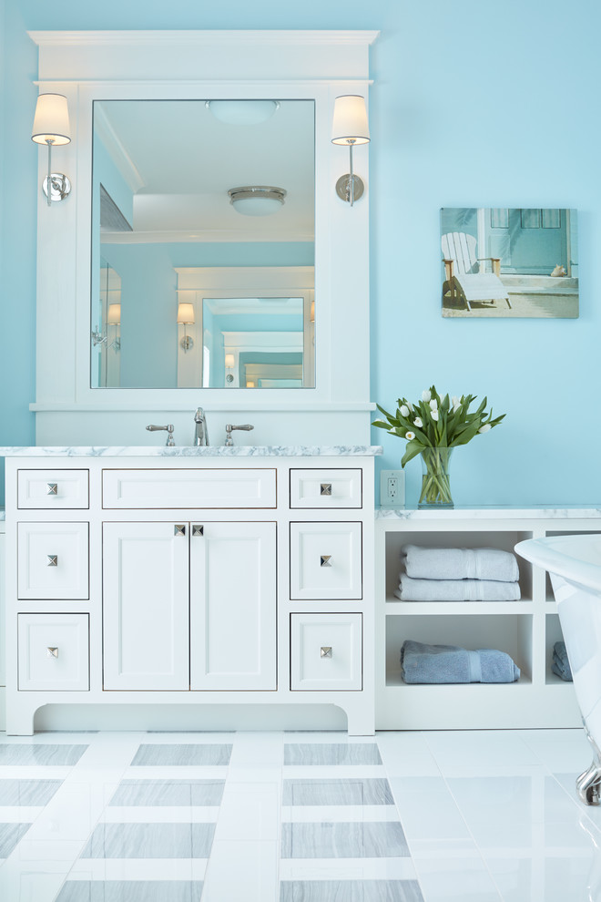 This is an example of a beach style master bathroom in Baltimore with white cabinets, a freestanding tub, white tile, blue walls, ceramic floors, a drop-in sink, granite benchtops and recessed-panel cabinets.