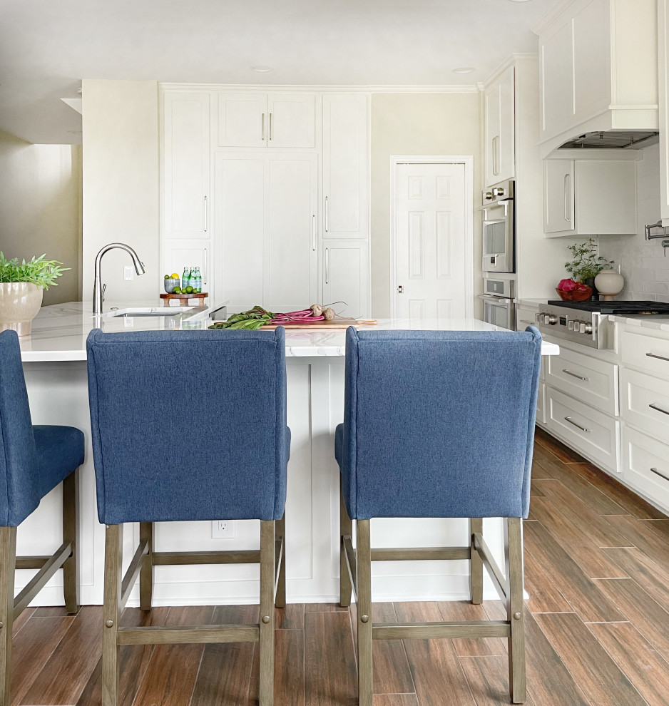 Example of a large ceramic tile and brown floor kitchen design in Austin with an undermount sink, shaker cabinets, white cabinets, white backsplash, subway tile backsplash, stainless steel appliances, an island and white countertops
