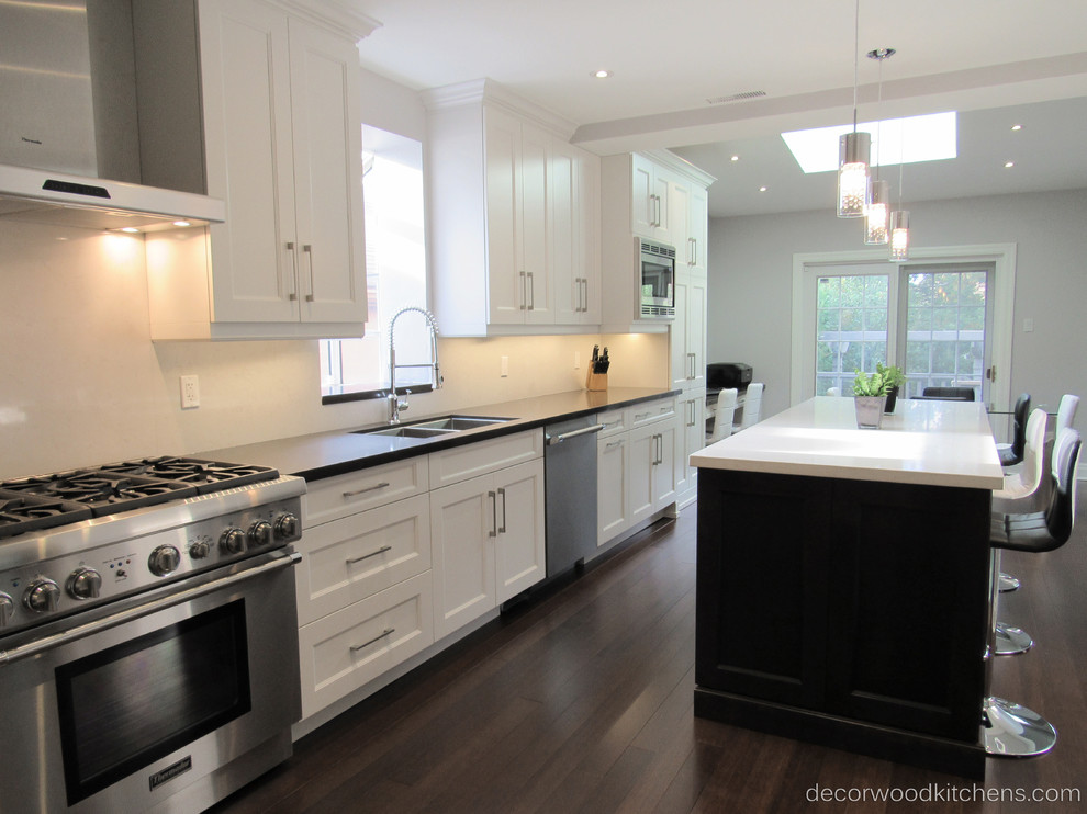 Inspiration for a large transitional l-shaped dark wood floor enclosed kitchen remodel in Toronto with an undermount sink, shaker cabinets, white cabinets, quartz countertops, white backsplash, stone slab backsplash, stainless steel appliances and an island