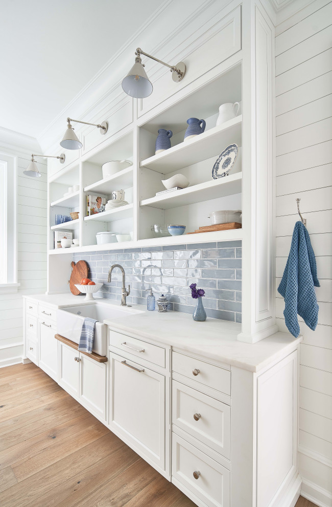 Design ideas for a nautical kitchen pantry in Charlotte with a belfast sink, beaded cabinets, white cabinets, marble worktops, white splashback, marble splashback, stainless steel appliances, medium hardwood flooring, multiple islands, brown floors, white worktops and a timber clad ceiling.