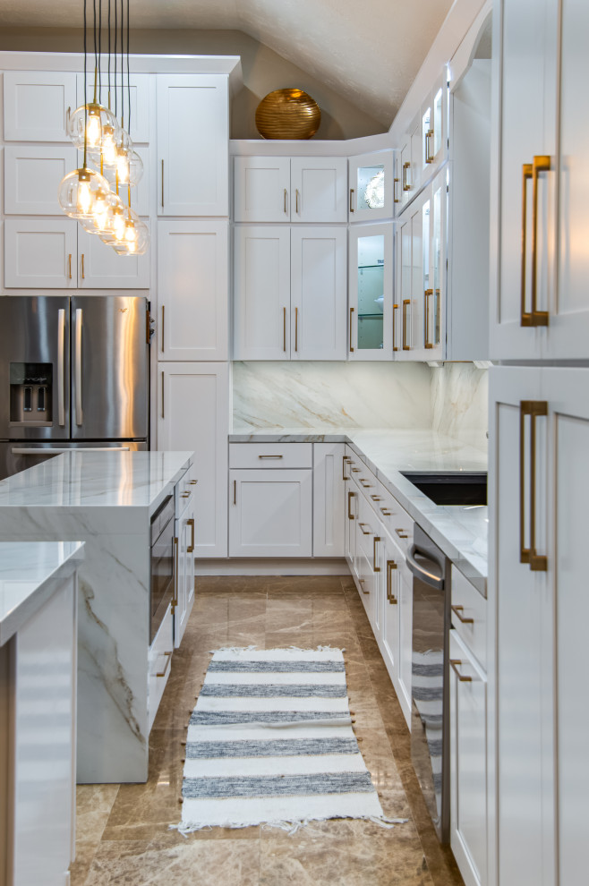 This is an example of a large modern l-shaped eat-in kitchen in Houston with an undermount sink, shaker cabinets, white cabinets, solid surface benchtops, white splashback, porcelain splashback, stainless steel appliances, marble floors, with island, beige floor and white benchtop.