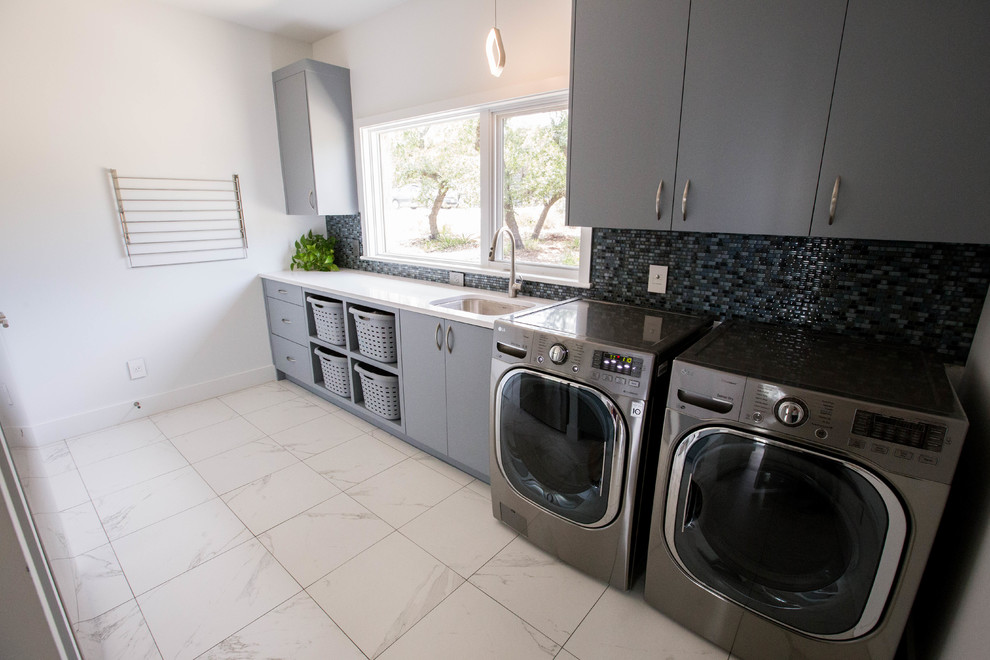 This is an example of a large modern galley utility room in Austin with an undermount sink, flat-panel cabinets, grey cabinets, quartz benchtops, white walls, marble floors, a side-by-side washer and dryer, white floor and white benchtop.