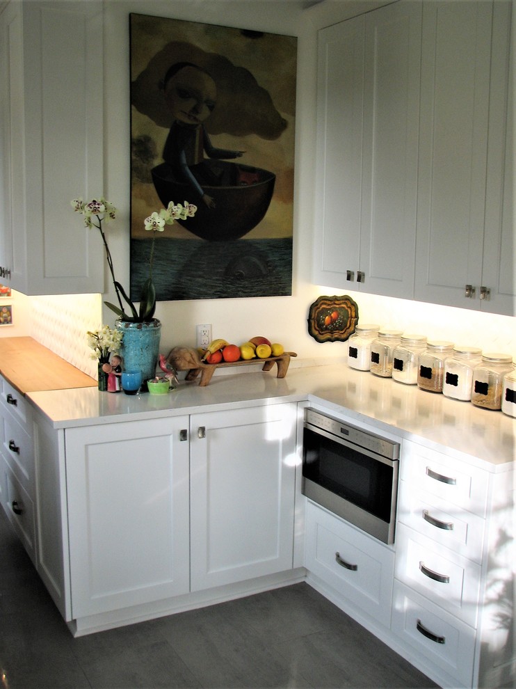This is an example of a small transitional galley separate kitchen in Seattle with a triple-bowl sink, shaker cabinets, white cabinets, quartz benchtops, white splashback, porcelain splashback, stainless steel appliances, medium hardwood floors, no island and brown floor.