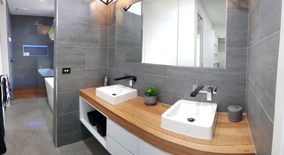 Photo of a mid-sized contemporary master bathroom in Geelong with flat-panel cabinets, white cabinets, a freestanding tub, a curbless shower, ceramic tile, grey walls, terrazzo floors, a vessel sink, wood benchtops, grey floor and a hinged shower door.