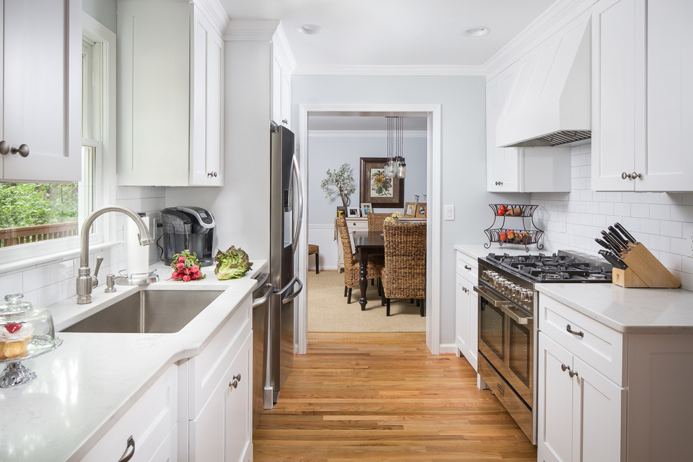 Small traditional galley eat-in kitchen in Atlanta with an undermount sink, shaker cabinets, white cabinets, quartz benchtops, white splashback, ceramic splashback, stainless steel appliances and light hardwood floors.