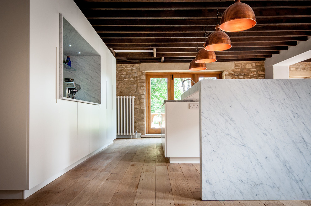 Photo of a large traditional single-wall open plan kitchen in London with an integrated sink, flat-panel cabinets, white cabinets, marble worktops, grey splashback, glass sheet splashback, stainless steel appliances, medium hardwood flooring and an island.