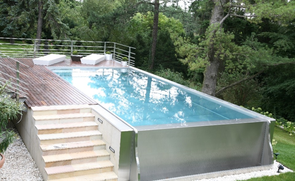 Exempel på en stor modern rektangulär pool längs med huset, med trädäck