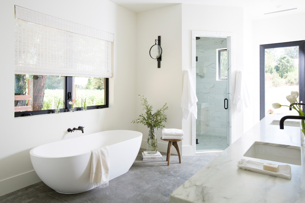 This is an example of a contemporary bathroom in San Francisco with a freestanding tub, an alcove shower, white walls, an undermount sink, marble benchtops, grey floor, a hinged shower door and white benchtops.