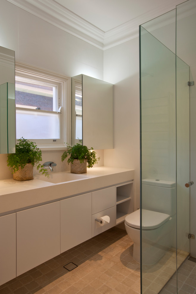 Large transitional kids bathroom in Sydney with an integrated sink, flat-panel cabinets, white cabinets, solid surface benchtops, a one-piece toilet, beige tile, stone tile and white walls.