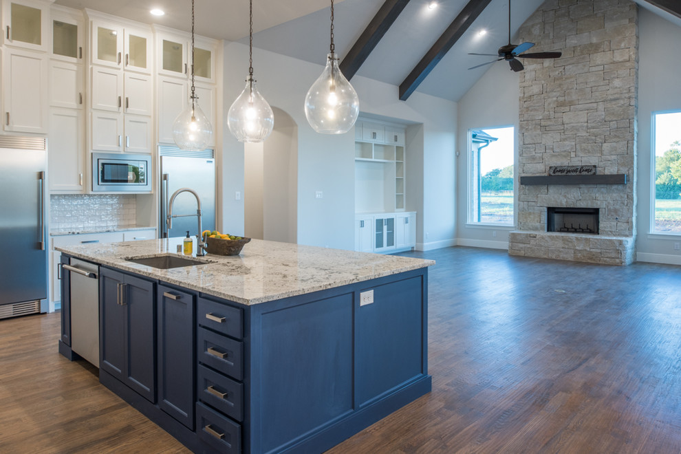 Open concept kitchen - large transitional u-shaped medium tone wood floor and brown floor open concept kitchen idea in Dallas with a drop-in sink, recessed-panel cabinets, white cabinets, granite countertops, white backsplash, ceramic backsplash, stainless steel appliances, an island and gray countertops