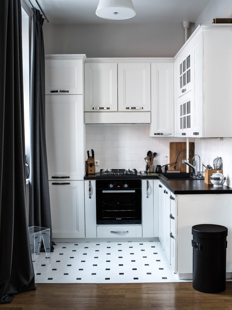 Small traditional l-shaped open plan kitchen in Other with a drop-in sink, white cabinets, white splashback, ceramic splashback, black appliances, ceramic floors, no island, recessed-panel cabinets, wood benchtops and white floor.