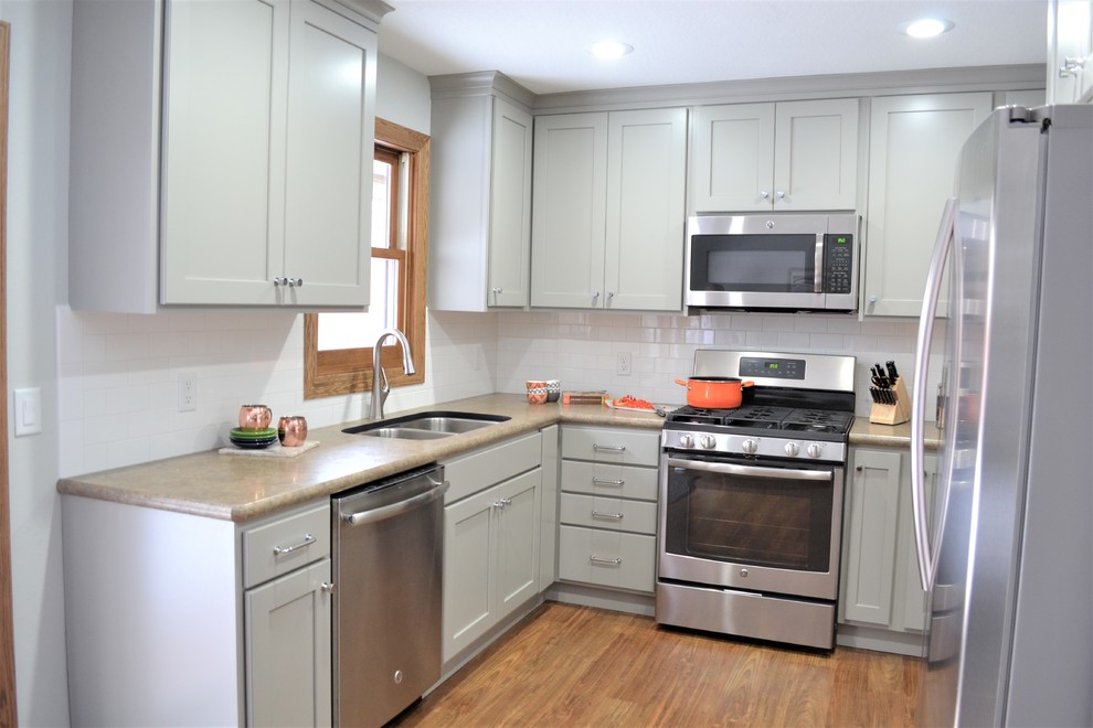Example of a mid-sized transitional u-shaped vinyl floor and brown floor enclosed kitchen design with an undermount sink, flat-panel cabinets, gray cabinets, laminate countertops, white backsplash, subway tile backsplash, stainless steel appliances and no island