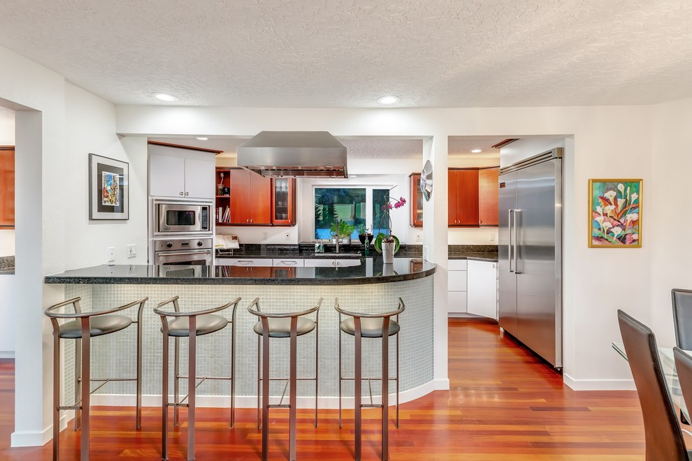 Mid-sized modern galley eat-in kitchen in Portland with a single-bowl sink, flat-panel cabinets, white cabinets, granite benchtops, white splashback, stone slab splashback, stainless steel appliances, dark hardwood floors, red floor and black benchtop.