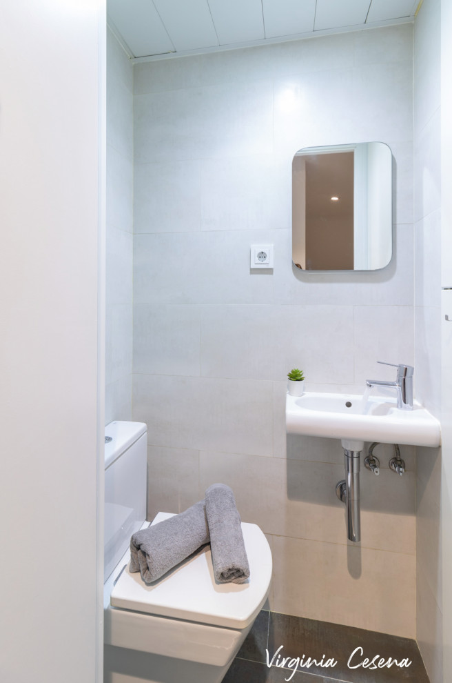 Diseño de aseo nórdico con puertas de armario grises, sanitario de una pieza, baldosas y/o azulejos blancos, baldosas y/o azulejos de cerámica, paredes blancas, suelo de baldosas de porcelana, lavabo suspendido, suelo gris y encimeras blancas