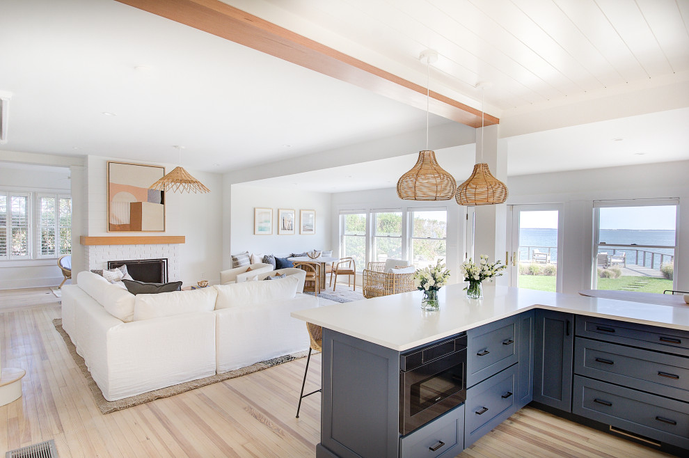 Design ideas for a mid-sized beach style open plan kitchen in Other with a farmhouse sink, recessed-panel cabinets, blue cabinets, quartz benchtops, white splashback, ceramic splashback, stainless steel appliances, light hardwood floors, with island, white benchtop and timber.