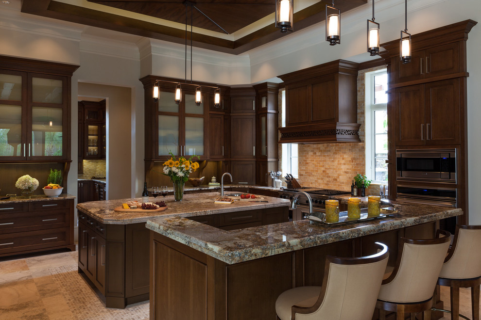 This is an example of a mediterranean kitchen in Miami with recessed-panel cabinets, dark wood cabinets, beige splashback, stainless steel appliances and multiple islands.