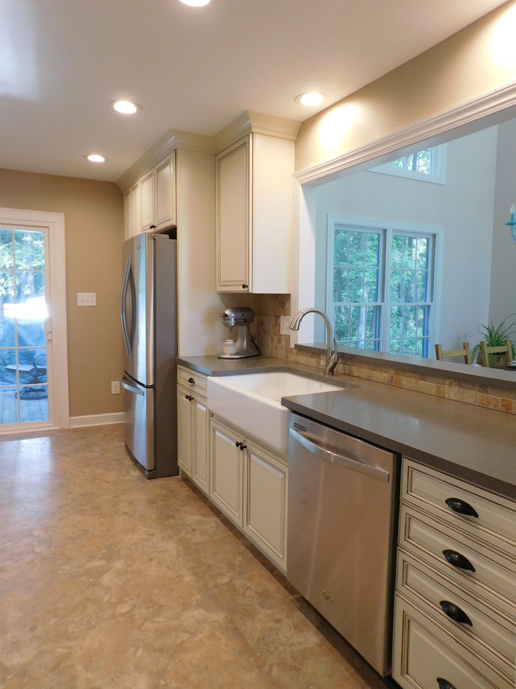 Mid-sized transitional galley vinyl floor enclosed kitchen photo with a farmhouse sink, raised-panel cabinets, beige cabinets, solid surface countertops, multicolored backsplash, stone tile backsplash, stainless steel appliances and no island
