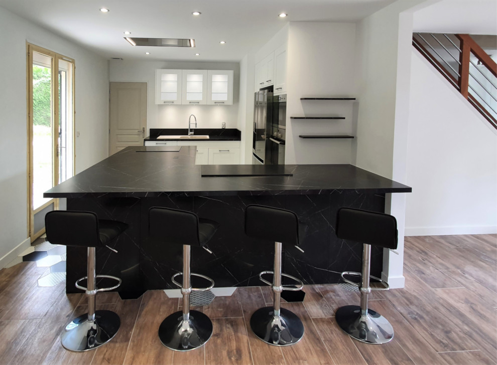 Photo of a large contemporary u-shaped open plan kitchen in Other with an undermount sink, flat-panel cabinets, stainless steel cabinets, granite benchtops, black splashback, granite splashback, panelled appliances, ceramic floors, with island, white floor and black benchtop.