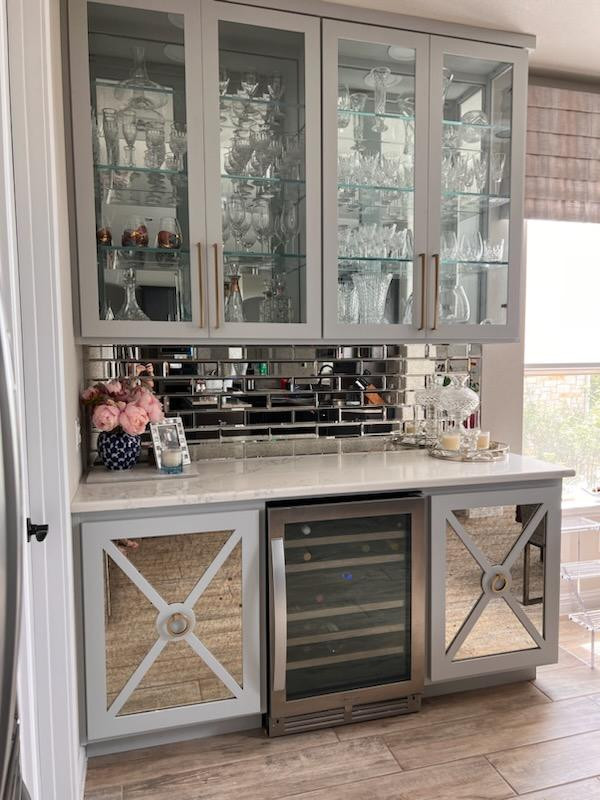 Small transitional medium tone wood floor dry bar photo in Austin with glass-front cabinets, gray cabinets, quartz countertops, mirror backsplash and white countertops